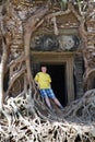 Young man, the teenager at an entrance to the destroyed covered with roots of trees temple Prasat Chrap in the Koh Ker temple comp