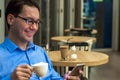 Young man texting in the cafe. Happy businessman smiling and texting on the smartphone at the table Royalty Free Stock Photo