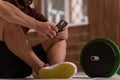 Young man texting sitting on a floor with smartphone, black and green tone fitness barbell, equipment for weight