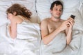 Young man is texting with someone using phone while his wife is sleeping near him.