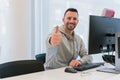 Young man with thumbs up happy and smiling for having achieved his goals in the office in front of the computer Royalty Free Stock Photo