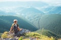 Young man tourist backpacker sits on top on hill with beautiful