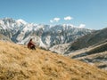 Young man tourist sits in mountain and look into distance. Snowy peaks background. Wild life travel concept