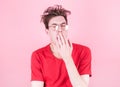 Young man with tousled hair yawns from fatigue against a pink background. Stress, fatigue and sleep concept