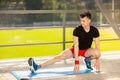 Young man training yoga outdoors. Sporty guy makes stretching exercise on a blue yoga mat, on the sports ground