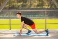 Young man training yoga outdoors. Sporty guy makes stretching exercise on a blue yoga mat, on the sports ground