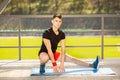 Young man training yoga outdoors. Sporty guy makes stretching exercise on a blue yoga mat, on the sports ground