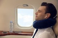 Young man with travel pillow resting while listening to music in airplane during flight Royalty Free Stock Photo