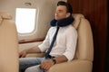 Young man with travel pillow resting while listening to music in airplane during flight Royalty Free Stock Photo