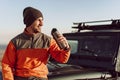 Young man traveler drinking from his thermocup while halt on a hike