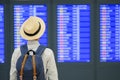 Young man traveler with hat checking flight time, Asian passenger looking to information board in international airport terminal.