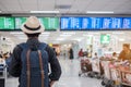 Young man traveler with hat checking flight time, Asian passenger looking to information board in international airport terminal. Royalty Free Stock Photo