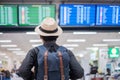 Young man traveler with hat checking flight time, Asian passenger looking to information board in international airport terminal. Royalty Free Stock Photo