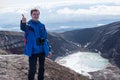 Young man traveler photographer at the top of the volcano mountain shows excellent, rejoices, volcanic view in the crater of the v Royalty Free Stock Photo