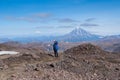 Young man traveler photographer at the top of the volcano mountain shows excellent, rejoices, volcanic view in the crater of the v Royalty Free Stock Photo