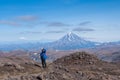 Young man traveler photographer at the top of the volcano mountain shows excellent, rejoices, volcanic view in the crater of the v Royalty Free Stock Photo