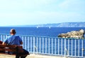 A young man traveler sitting on a bench on Mediterranean coast on promenade of Marseille. Back view of beautiful sea panorama and Royalty Free Stock Photo