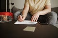 Young man traveler is sitting on couch and filling documents in hotel room on summer vacation. Cool male in casual