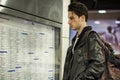 Young man traveling, reading train timetable in railway station