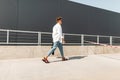 Young man with a trendy hairstyle in a white shirt in vintage blue jeans in leather sandals with a black bag walks down the street Royalty Free Stock Photo
