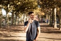 Young man in tshirt standing on street, speaks on a mobile phone and smiles. In the background is a tree lane Royalty Free Stock Photo