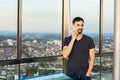 Young man in tshirt stands on the observation deck with large windows and speaks on a mobile phone Royalty Free Stock Photo