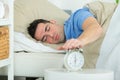 Young man turning off alarm clock on bed Royalty Free Stock Photo