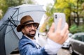 Young man with umbrella making video for social media outdoors on street. Royalty Free Stock Photo