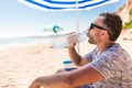 Young man under solar umbrella drink water from cooler on sea beach Royalty Free Stock Photo