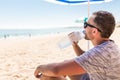 Young man under solar umbrella drink water from cooler on sea beach Royalty Free Stock Photo