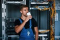 Young man in uniform drinking coffee against internet equipment and wires in server room