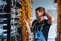 Young man in uniform feels confused and looking for a solution with internet equipment and wires in server room