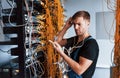 Young man in uniform feels confused and looking for a solution with internet equipment and wires in server room