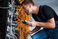 Young man in uniform with measuring device works with internet equipment and wires in server room