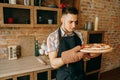 Young man unskilled cook look at self-cooked pizza