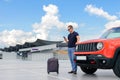 A young man uses a smartphone while standing near a car in an open parking lot. Road lifestyle concept