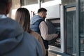 Young man using cash machine for money withdrawal outdoors. ATM queue Royalty Free Stock Photo