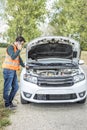 Young man using his cell phone in front of a broken down car Royalty Free Stock Photo