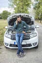 Young man using his cell phone in front of a broken down car Royalty Free Stock Photo