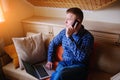 Young man using his smartphone for online banking - sitting on sofa with laptop on leap Royalty Free Stock Photo