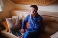 Young man using his smartphone for online banking - sitting on sofa with laptop on leap Royalty Free Stock Photo