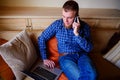 Young man using his smartphone for online banking - sitting on sofa with laptop on leap Royalty Free Stock Photo