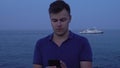Young man using his smartphone at sea seafront cruise ship motorship background at evening