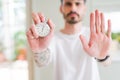Young man using holding stopwatch with open hand doing stop sign with serious and confident expression, defense gesture Royalty Free Stock Photo