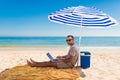 Young man using a laptop computer on the beach under solar umbrella. Freelance Concepts Royalty Free Stock Photo