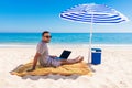 Young man using a laptop computer on the beach under umbrella. Freelance Concepts Royalty Free Stock Photo