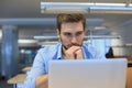 Young man using a laptop sitting thinking at his desk as he reads information on the screen Royalty Free Stock Photo