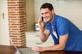 Young man using laptop and talking on phone Royalty Free Stock Photo