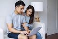 Man using laptop working online while sitting on sofa with his girlfriend together in living room. Sweet couple shopping Royalty Free Stock Photo