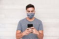 Young man using mobile phone app while wearing protective face mask during coronavirus outbreak - Millennial guy wathing videos on